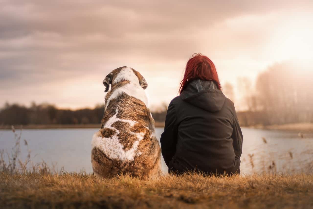 woman sitting with a dog along a river