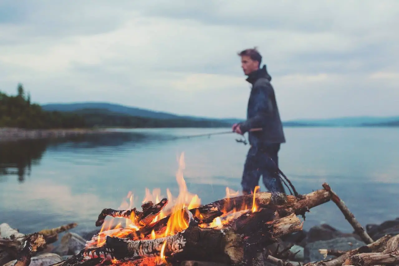 a guy camping besides a lake and a bonfire